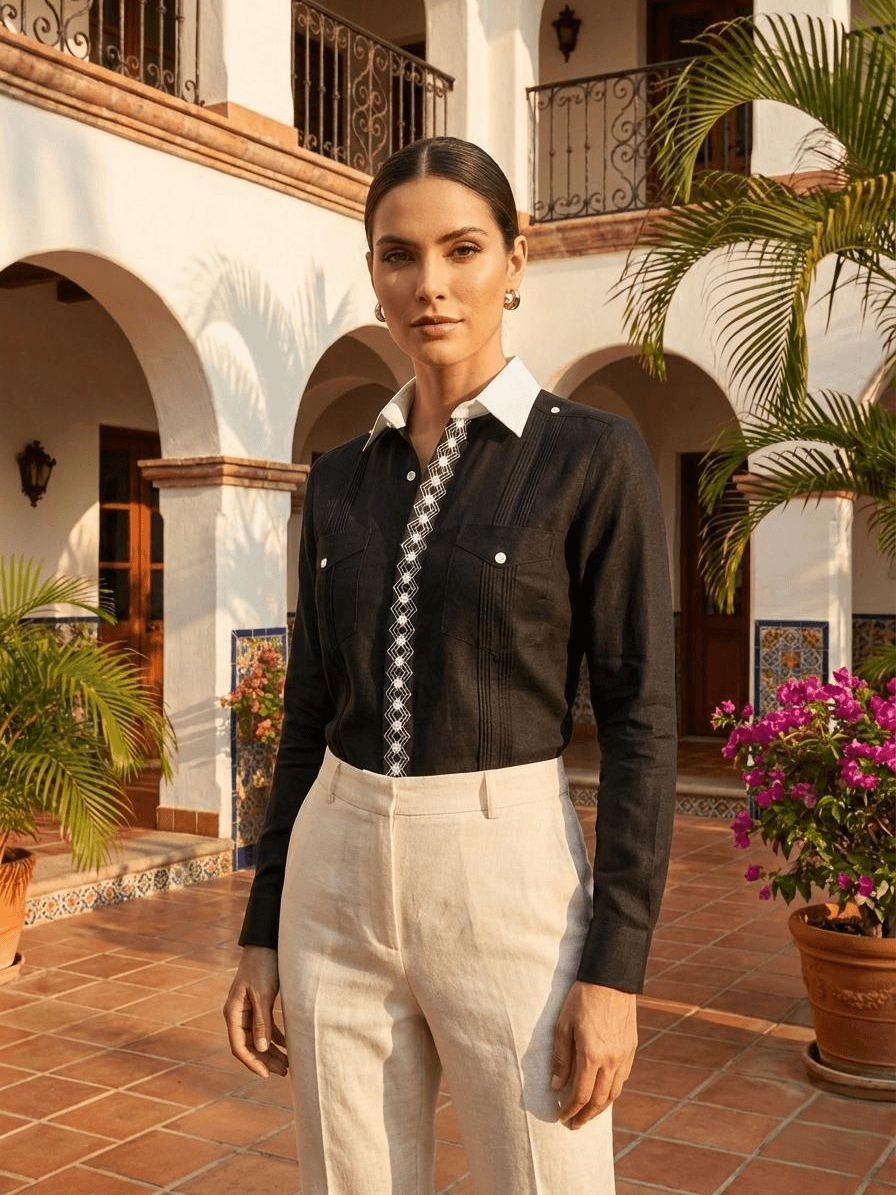Camisa guayabera negra de manga larga con una franja central de bordado geométrico blanco y cuatro bolsillos con botones blancos, presentada en un maniquí.