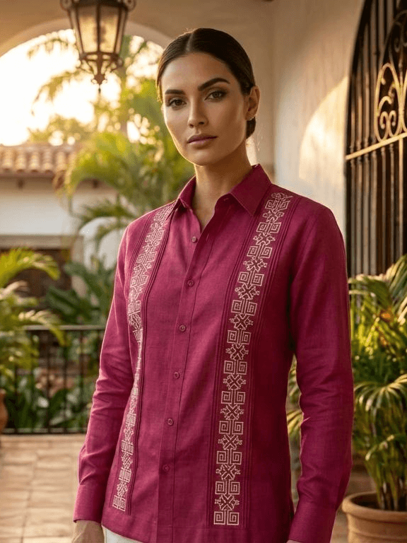 Camisa guayabera de manga larga en color rojo intenso con dos columnas de bordados geométricos de color crema, presentada en un maniquí sobre un fondo rústico.