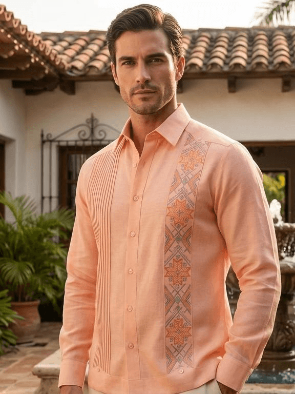 Camisa guayabera de manga larga en color salmón pálido con bordados de estrellas naranjas en un costado y pliegues verticales en el otro, presentada en un maniquí.