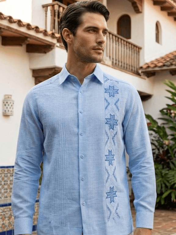 Camisa guayabera de manga larga en color azul claro con una franja de bordados de estrellas en azul oscuro y pliegues verticales, exhibida en un maniquí.